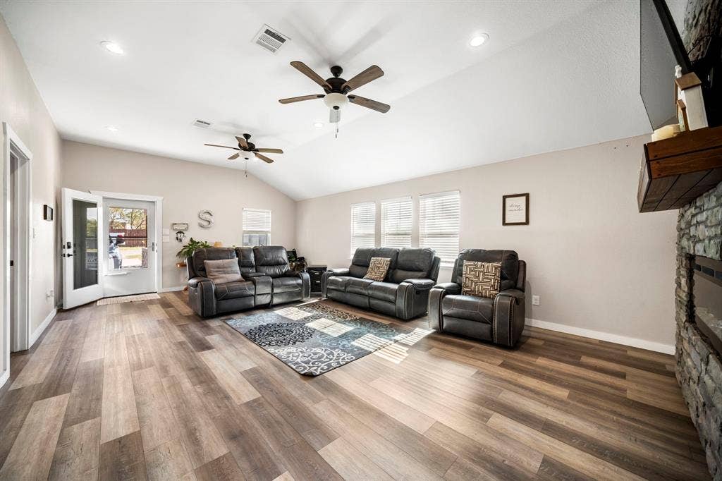 205 Newman Road, Ennis, TX 75119 Vaulted ceilings, wood-finish flooring, dual ceiling fans, recessed lighting, and a stone-faced fireplace with a wooden mantel
