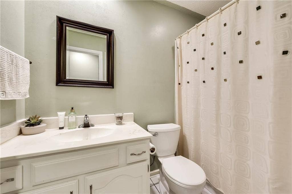 3702 Pulsar Drive, Garland, TX 75044 Bathroom featuring a white vanity with integrated basin, solid-surface countertop, dark-framed wall mirror, and porcelain toilet