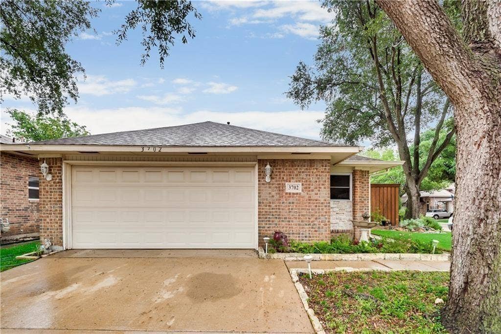 3702 Pulsar Drive, Garland, TX 75044 Brick exterior featuring an attached two-car garage, concrete driveway, stone accents, and shingled roof