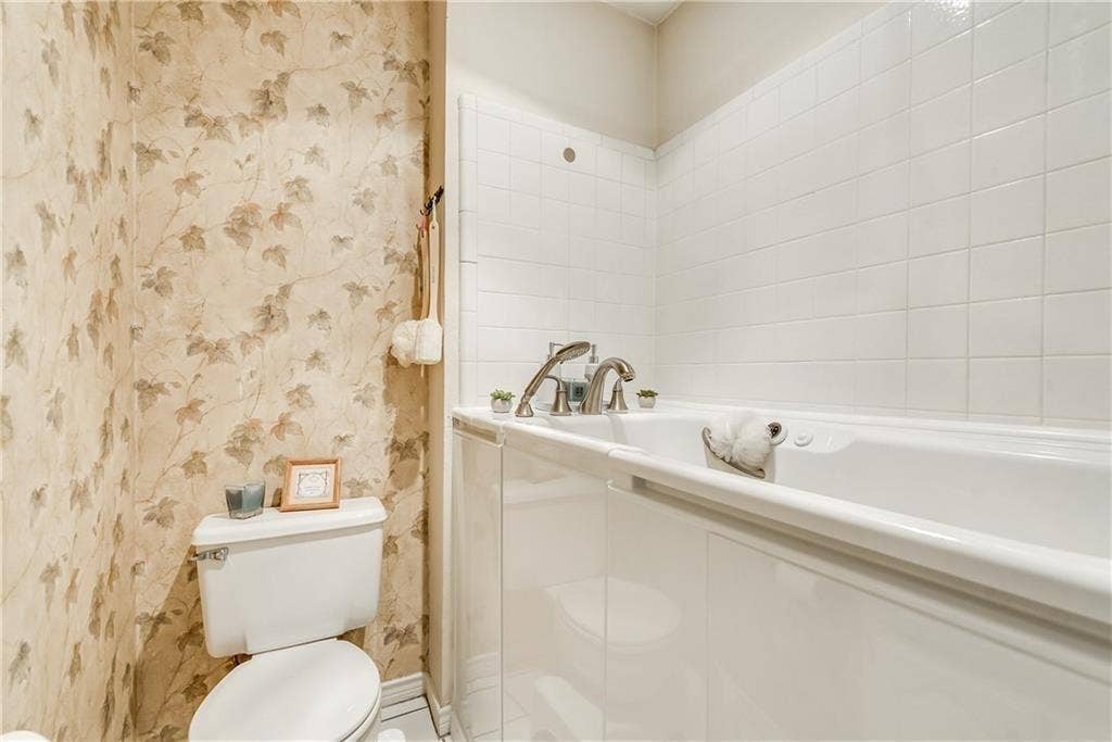 3702 Pulsar Drive, Garland, TX 75044 Built-in soaking tub with metallic faucet fixtures, white subway-style tile surround, and dual-flush toilet