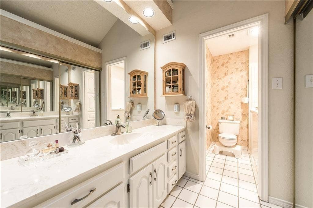 3702 Pulsar Drive, Garland, TX 75044 Full-width vanity featuring a solid surface countertop, integrated sink, white cabinetry, wall-to-wall mirror, and wall-mounted wooden storage cabinet