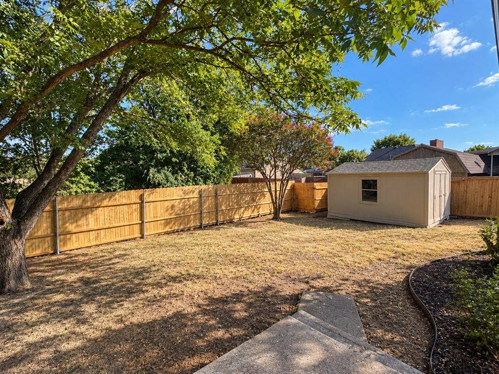 1412 Kaylor Drive, DeSoto, TX 75115 Backyard featuring a perimeter wood fence, detached storage structure, concrete pathway, mature trees, and ground cover