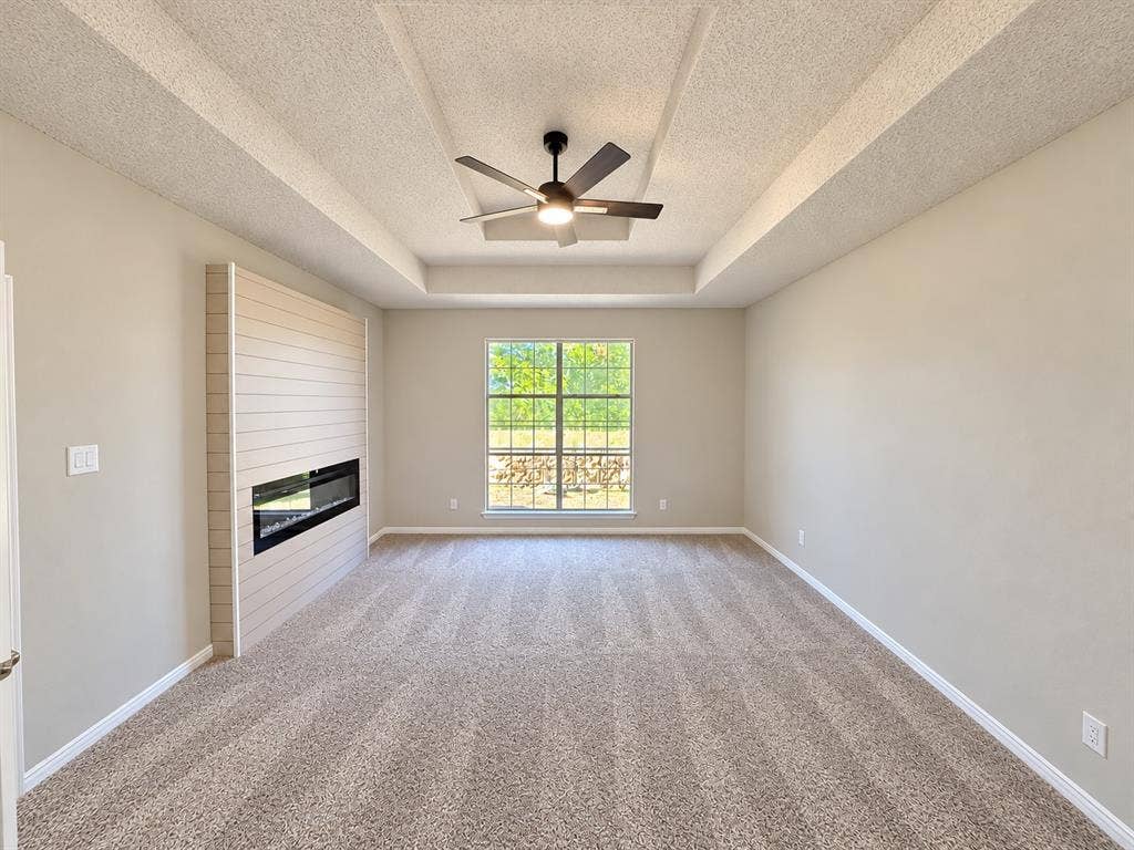 1412 Kaylor Drive, DeSoto, TX 75115 Tray ceiling featuring a central lighted ceiling fan, complemented by a horizontal shiplap fireplace surround and a wall-mounted linear electric fireplace