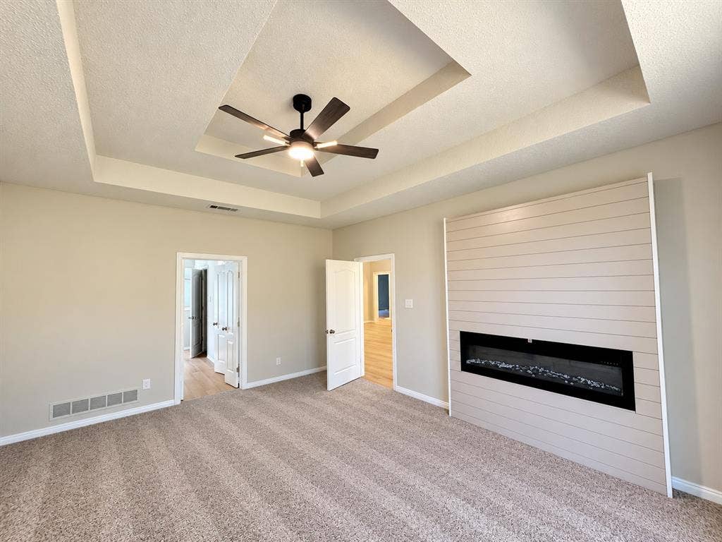 1412 Kaylor Drive, DeSoto, TX 75115 Tray ceiling with a central multi-blade ceiling fan, expansive shiplap accent wall, and integrated horizontal electric fireplace