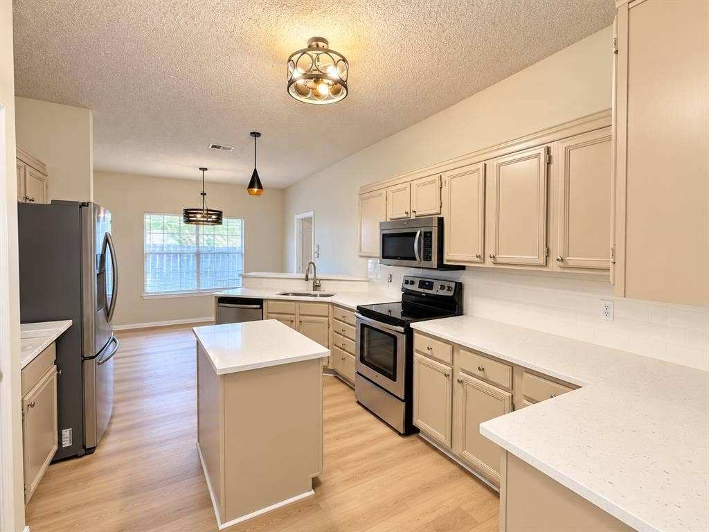 1412 Kaylor Drive, DeSoto, TX 75115 Kitchen featuring custom cabinetry, light-toned countertops, stainless steel appliances, a mobile center island, and wood-finish flooring