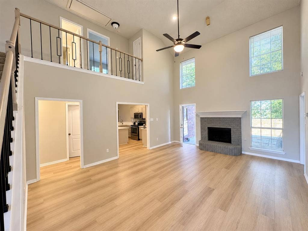 1412 Kaylor Drive, DeSoto, TX 75115 Double-height living area featuring wood-finish flooring, a brick fireplace with a decorative mantel, multiple large windows, and a metal-baluster staircase railing