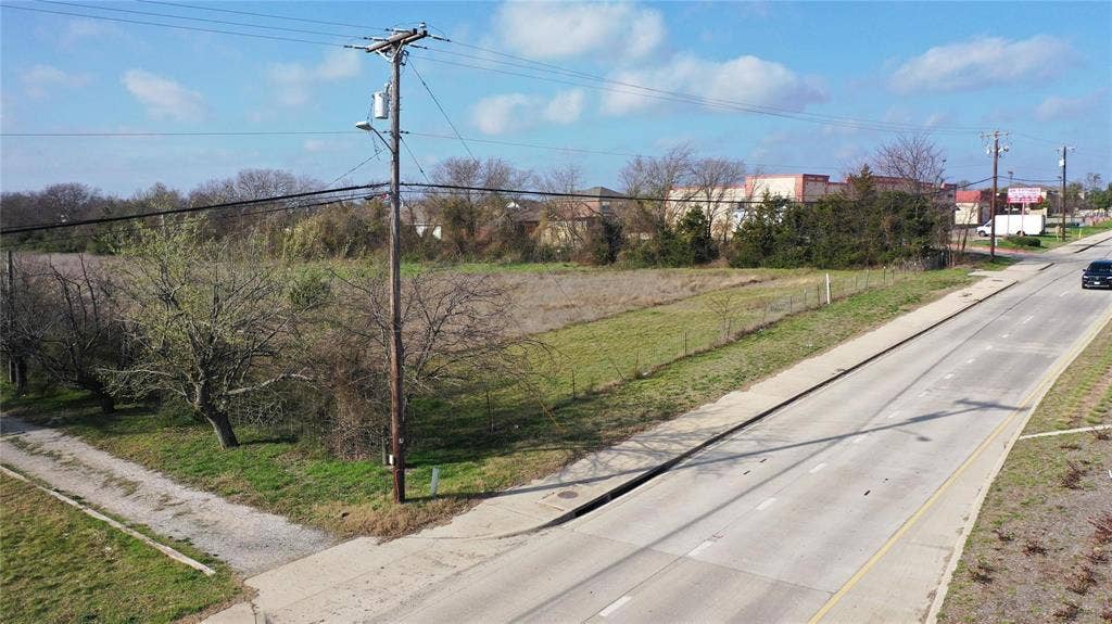 The property features a substantial undeveloped lot with a partial fence, mature trees, and direct frontage to a paved road