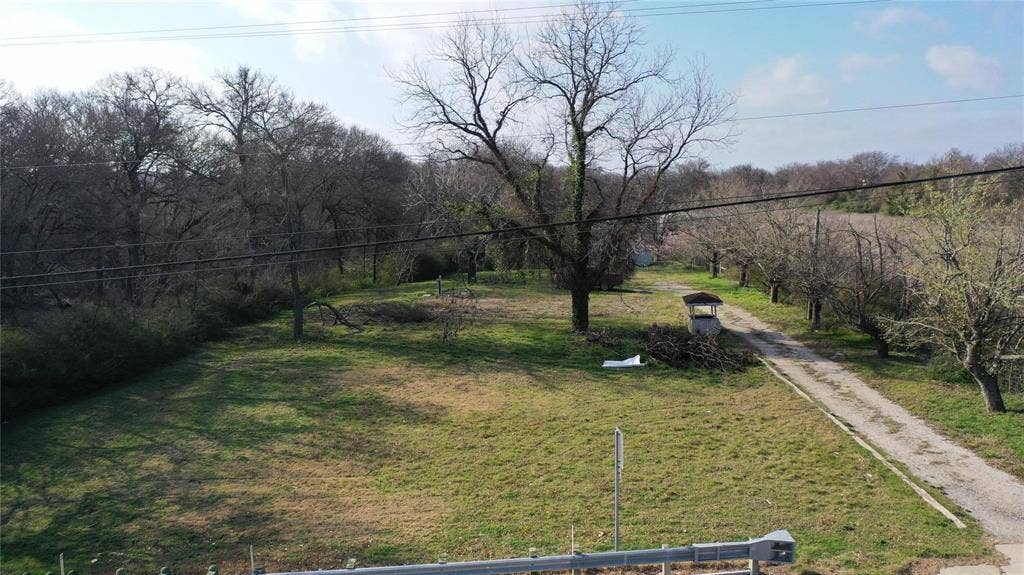 Expansive lot featuring a dirt driveway, mature trees, and a grassy area