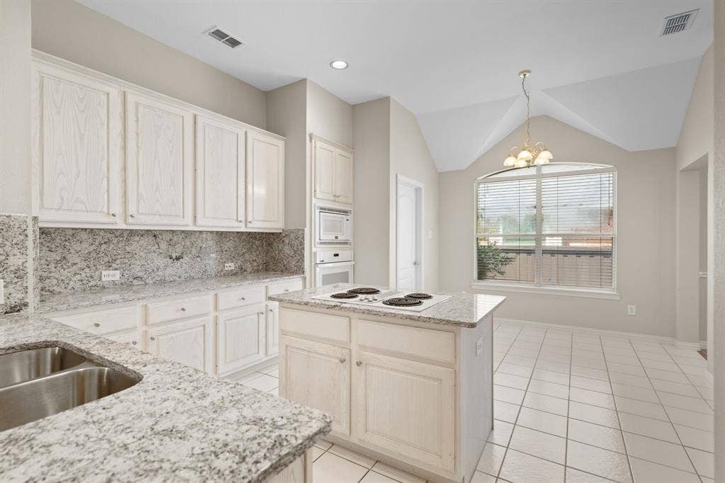 Kitchen featuring white appliances, light tile patterned floors, a chandelier, decorative backsplash, and vaulted ceiling