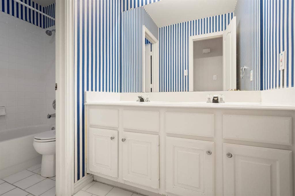 Full bath featuring tile patterned floors, wallpapered walls, double vanity, and shower / bath combination