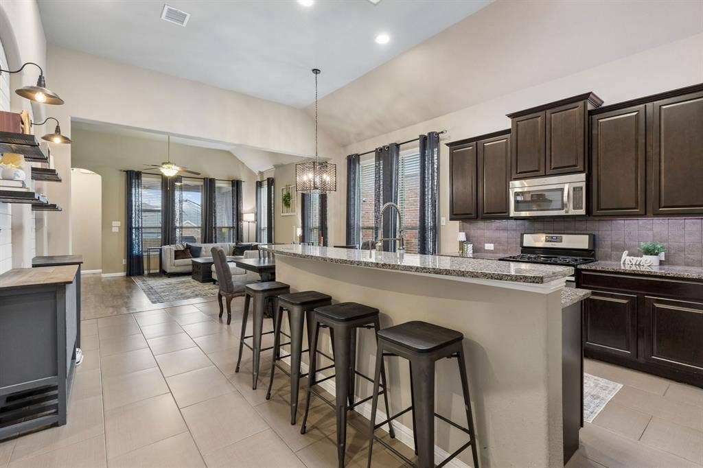 Welcome to the kitchen! Soaring ceilings, a spacious breakfast bar, and an open layout create a seamless flow into the dining and living areas.