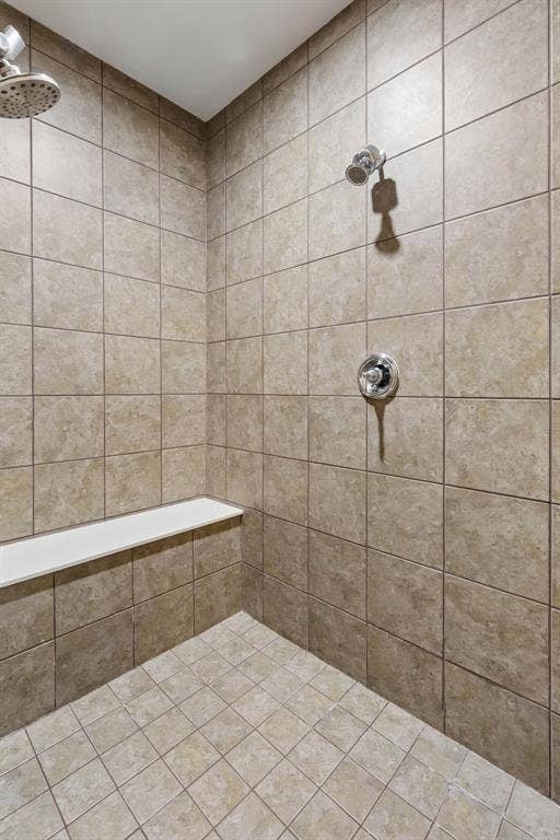 The spacious walk-in shower features a built-in bench, beautiful tile finishes, sleek chrome fixtures, and dual shower heads for added comfort.