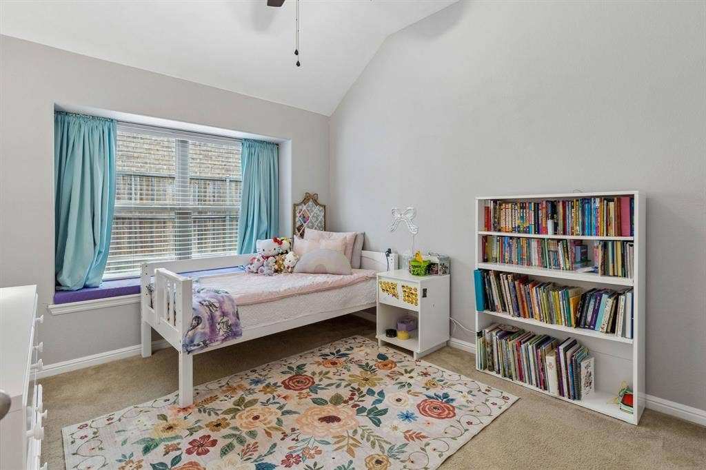 The second secondary bedroom offers cozy carpeting, a spacious walk-in closet, ceiling fan, charming window seat, and an arched ceiling, along with a large window that fills the room with natural light.