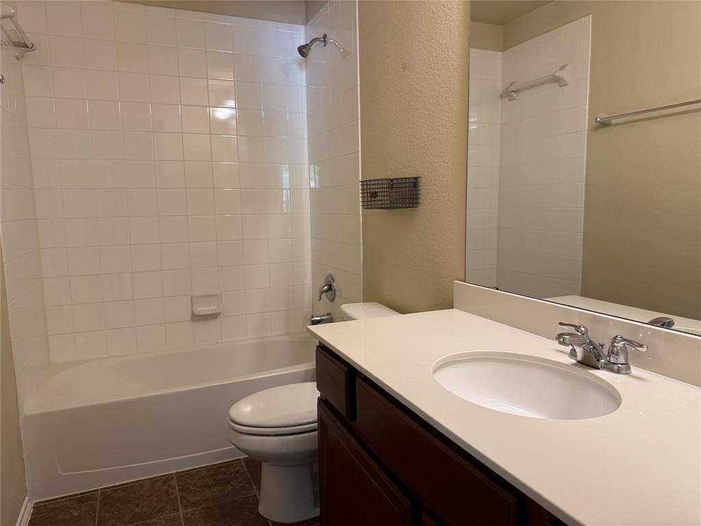 212 Belford Street S, Anna, TX 75409 Bathroom featuring a vanity with a light-toned solid surface countertop, an integrated oval sink, dark cabinetry, ceramic tile bathtub surround, and tile flooring