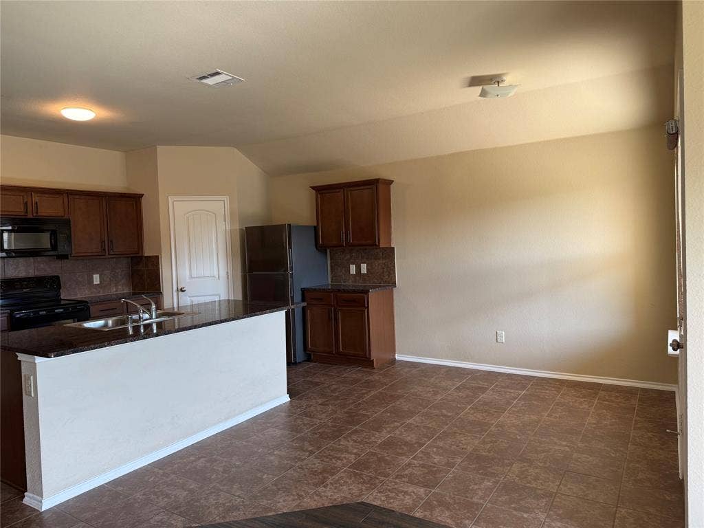 212 Belford Street S, Anna, TX 75409 Kitchen featuring stained wood cabinetry, stone-finish countertops, tile flooring, and a peninsula island with an integrated stainless steel sink