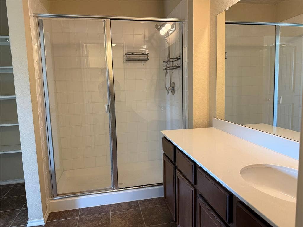 212 Belford Street S, Anna, TX 75409 Bathroom featuring a vanity with a white countertop and integrated sink, a glass-enclosed shower with tiled walls, built-in shelving, and dark-toned cabinetry