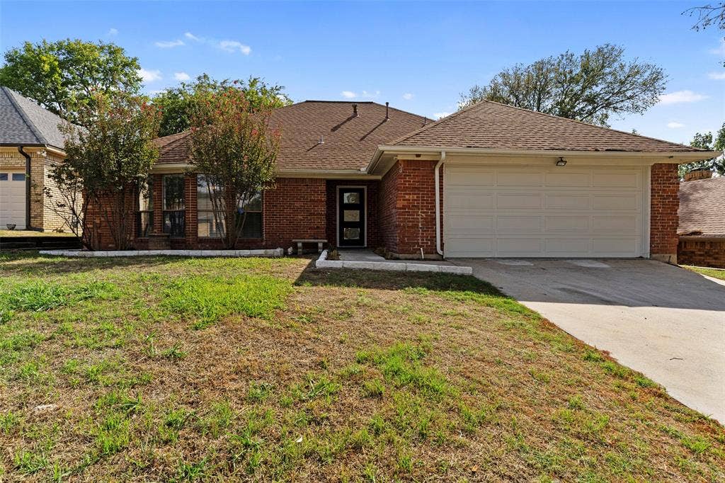 4128 Woodenrail Lane, Irving, TX 75061 Single-story brick exterior featuring a multi-gabled roofline, an attached two-car garage, and a covered entryway with a multi-pane glass door