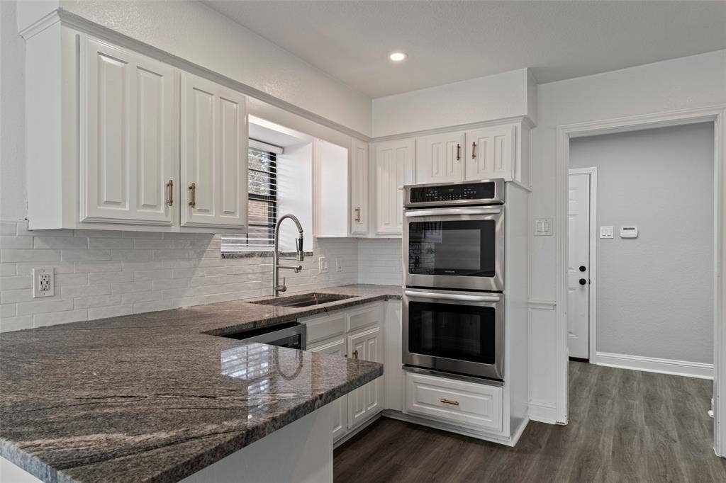 4128 Woodenrail Lane, Irving, TX 75061 Kitchen featuring granite countertops, white cabinetry with metallic hardware, subway tile backsplash, stainless steel double wall oven, and wood-finish flooring