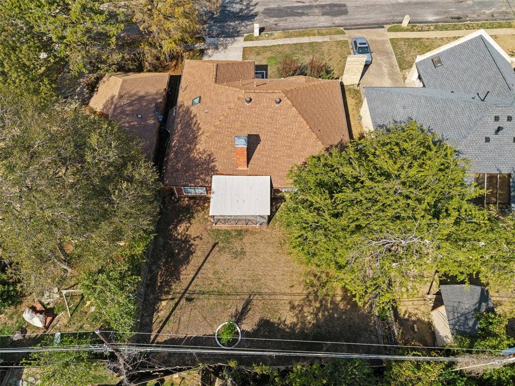4128 Woodenrail Lane, Irving, TX 75061 Aerial perspective of the residential lot featuring a multi-slope roofline, a centered masonry chimney, a screened rear patio structure, and mature tree coverage