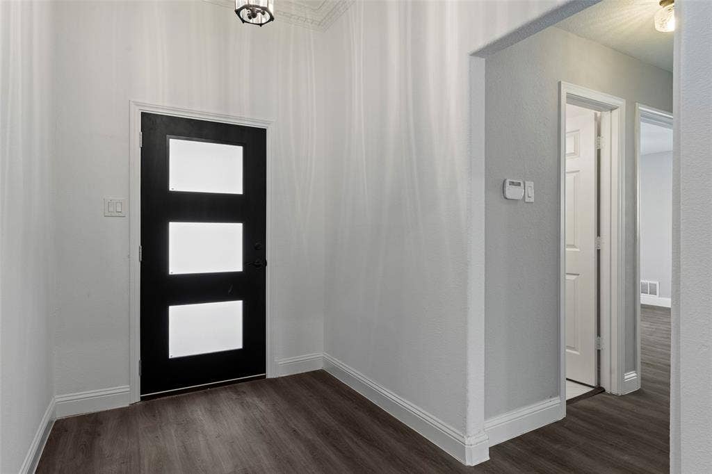 4128 Woodenrail Lane, Irving, TX 75061 Entryway featuring a black exterior-style door with three rectangular glass inserts, wood-finish flooring, neutral wall paint, and overhead decorative lighting