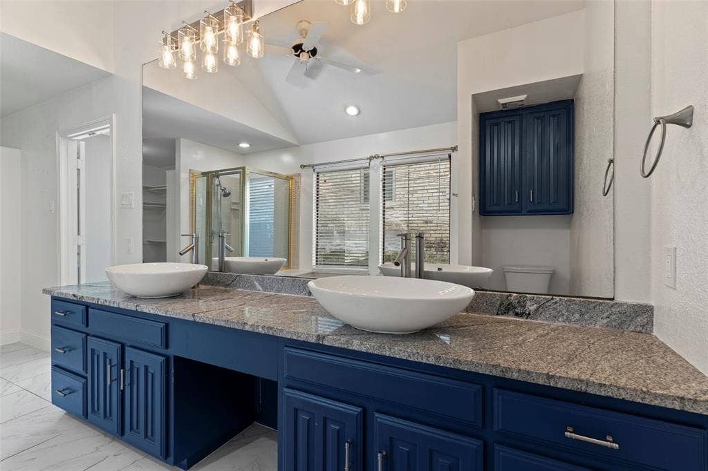 4128 Woodenrail Lane, Irving, TX 75061 Dual vanity featuring navy blue cabinetry, stone countertops, vessel sinks, chrome faucets, and a full-width mirror