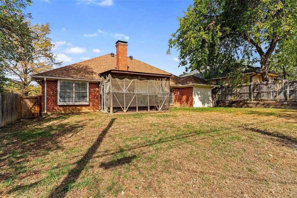 4128 Woodenrail Lane, Irving, TX 75061 Exterior backyard featuring a brick facade, screened porch, brick chimney, wood fence, and mature trees