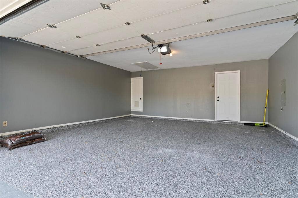 4128 Woodenrail Lane, Irving, TX 75061 Finished garage space featuring durable epoxy flooring, neutral wall paint, a metal panel overhead garage door, and a dedicated entry door