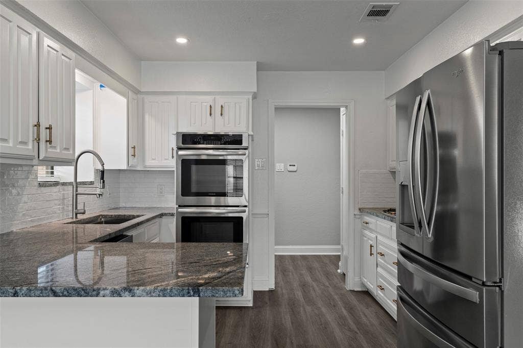 4128 Woodenrail Lane, Irving, TX 75061 Kitchen featuring white cabinetry with metallic pulls, granite countertops, stainless steel double wall ovens, stainless steel refrigerator, and wood-finish flooring