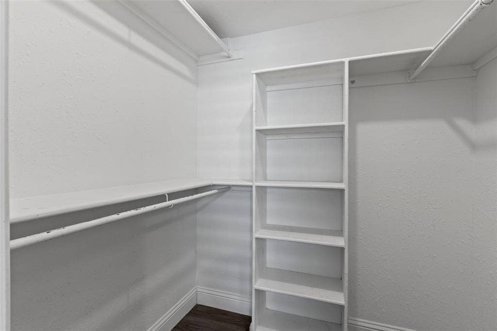 4128 Woodenrail Lane, Irving, TX 75061 Walk-in closet featuring white built-in shelving, dual-level hanging rods, and dark wood-finish flooring