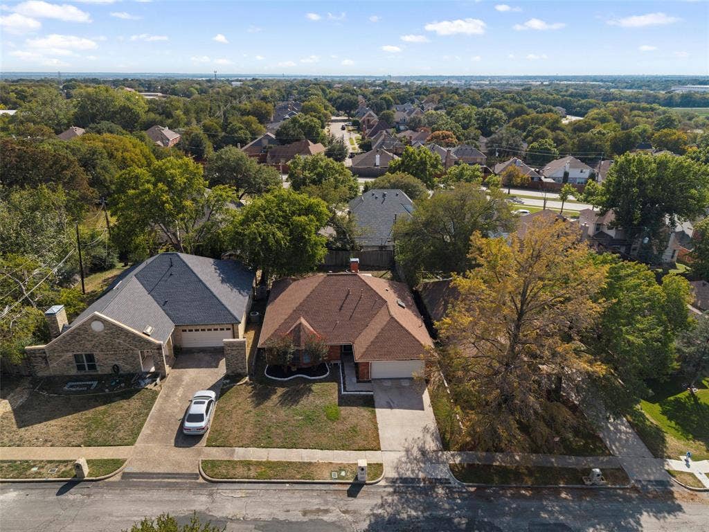 4128 Woodenrail Lane, Irving, TX 75061 Aerial perspective of residential properties featuring brick and masonry construction, multi-pitched shingle roofs, attached multi-car garages, concrete driveways, and established tree canopy
