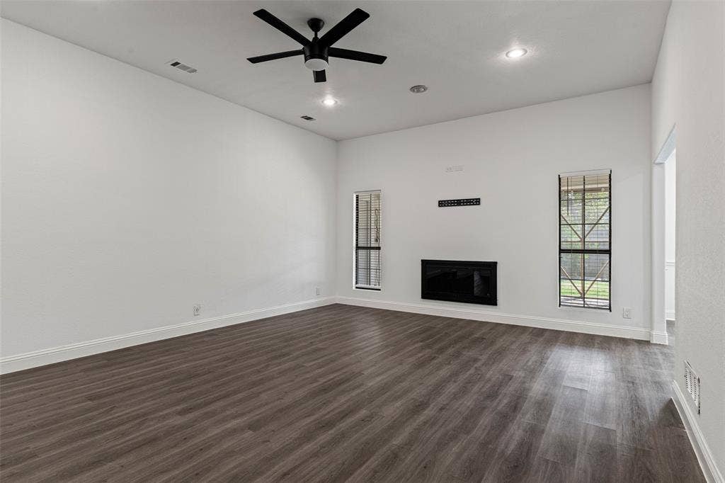 4128 Woodenrail Lane, Irving, TX 75061 High-ceilinged room featuring wood-finish flooring, a flush-mount fireplace, dual windows with grid detailing, and a matte black ceiling fan