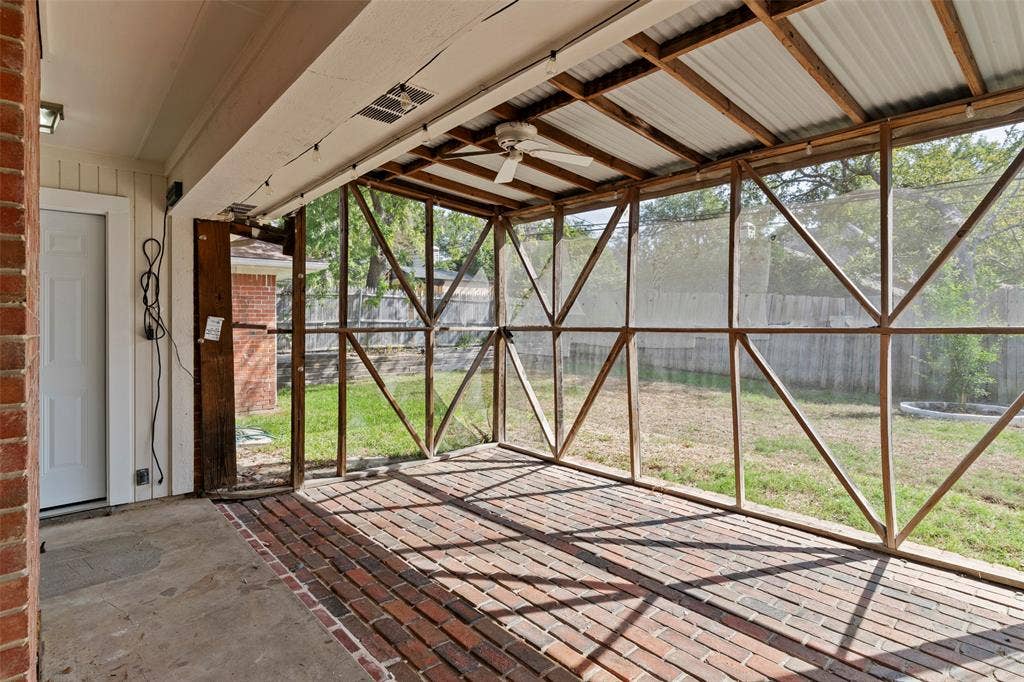 4128 Woodenrail Lane, Irving, TX 75061 Screened patio featuring a herringbone-patterned brick floor, exposed timber framing, corrugated metal ceiling, and a ceiling fan