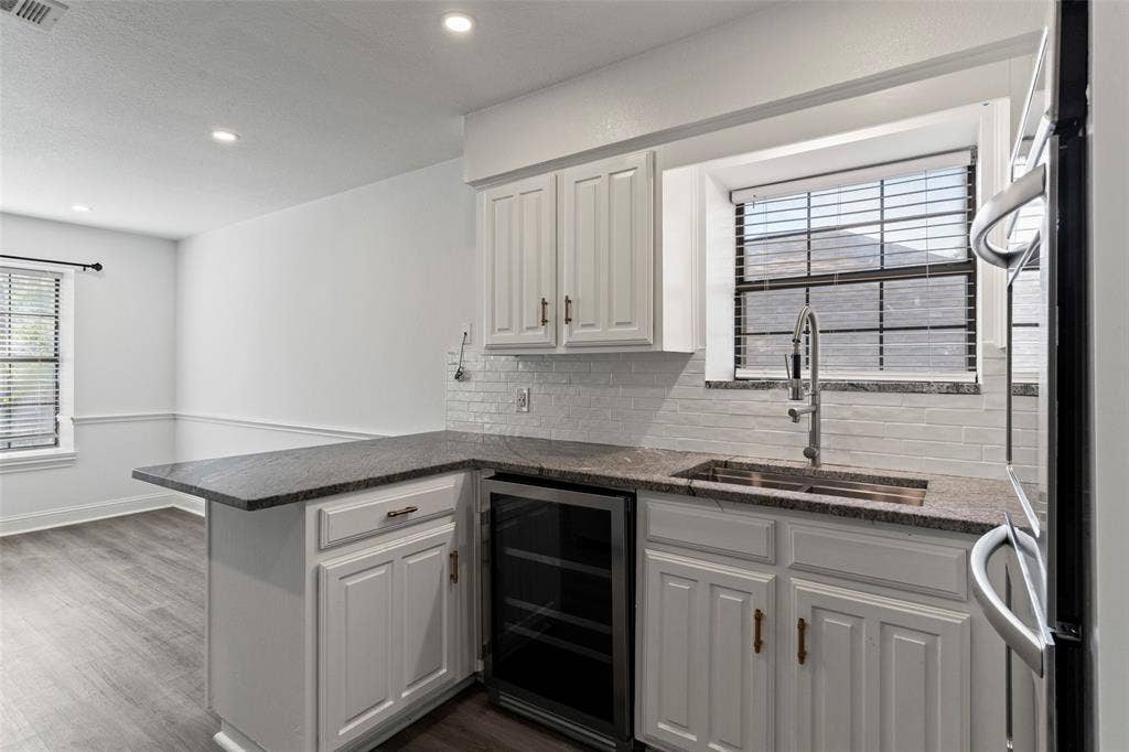 4128 Woodenrail Lane, Irving, TX 75061 Kitchen featuring white shaker-style cabinetry, granite countertops, a white subway-tile backsplash, a stainless steel undermount sink with a gooseneck faucet, and a built-in wine refrigerator