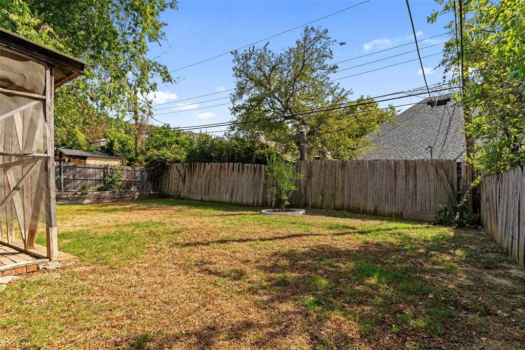 4128 Woodenrail Lane, Irving, TX 75061 Backyard featuring a wood-panel fence, mature trees, a screened-in structure, and open green space