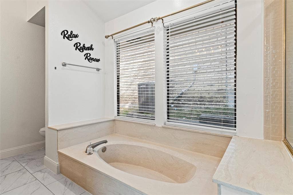 4128 Woodenrail Lane, Irving, TX 75061 Built-in soaking tub with surround stone-finish deck, dual windows with horizontal blinds, and large-format tile flooring