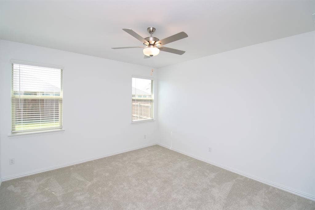 Neutral interior space featuring carpeted flooring, two windows with horizontal blinds, and a brushed-nickel ceiling fan with integrated lighting
