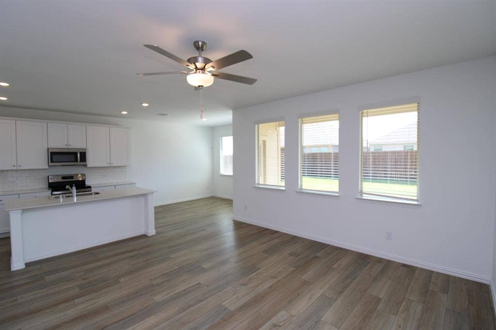 Kitchen featuring a central island with a stone countertop, white cabinetry, integrated stainless steel appliances, wood-finish flooring, and a ceiling fan with light fixture