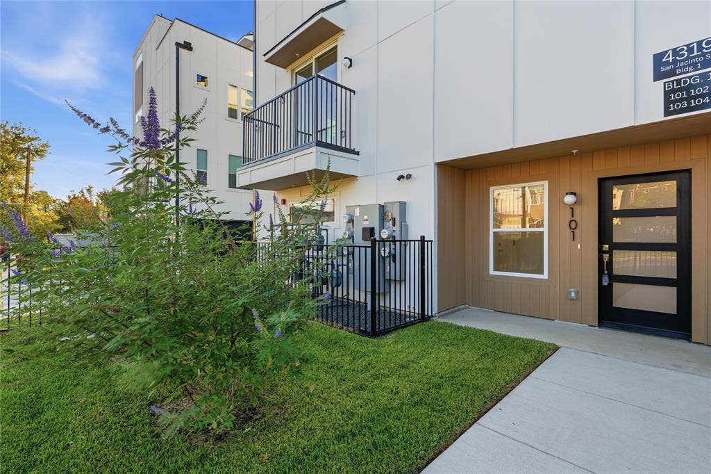 4319 San Jacinto Street, #101, Dallas, TX 75204 Modern exterior featuring white paneled siding, horizontal wood-toned accents, a second-story balcony with metal railings, and a contemporary glass-paneled front door