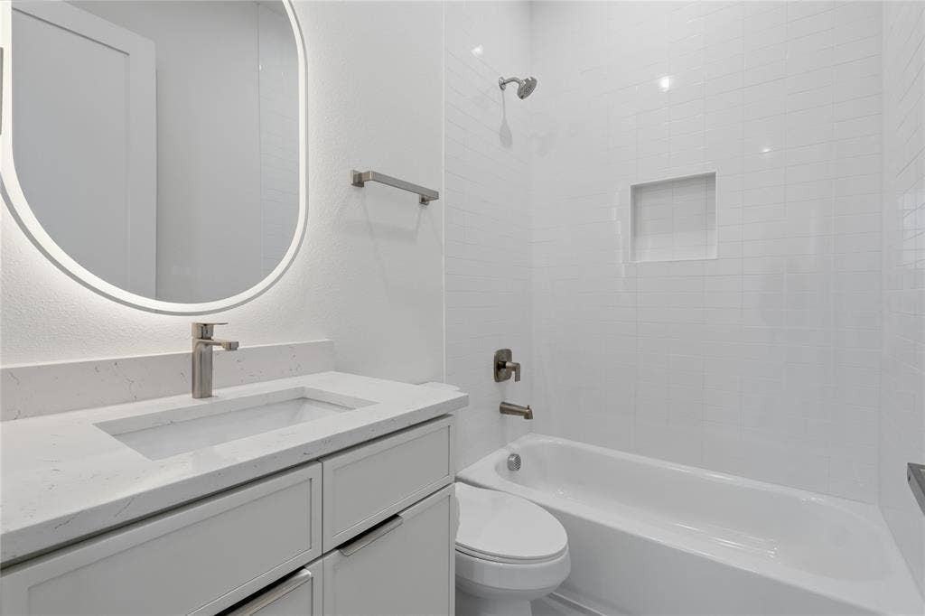 4319 San Jacinto Street, #101, Dallas, TX 75204 Bathroom featuring a vanity with a quartz countertop, integrated rectangular sink, backlit oval mirror, and a bathtub with a tiled surround and built-in niche