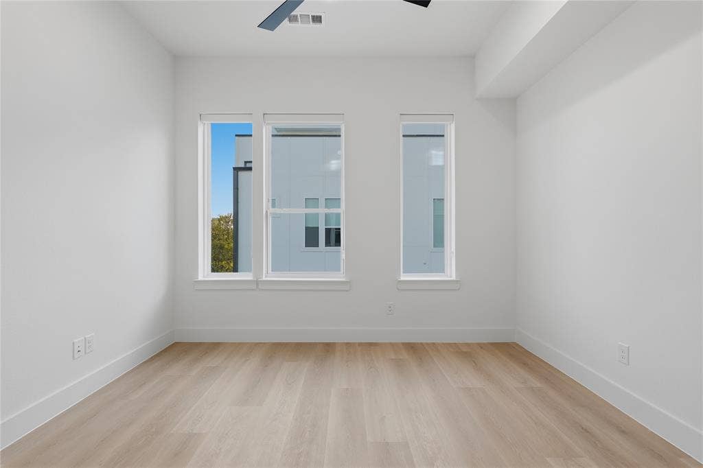 4319 San Jacinto Street, #101, Dallas, TX 75204 Neutral-toned space featuring wood-finish flooring, three oversized windows, and a ceiling-mounted fan