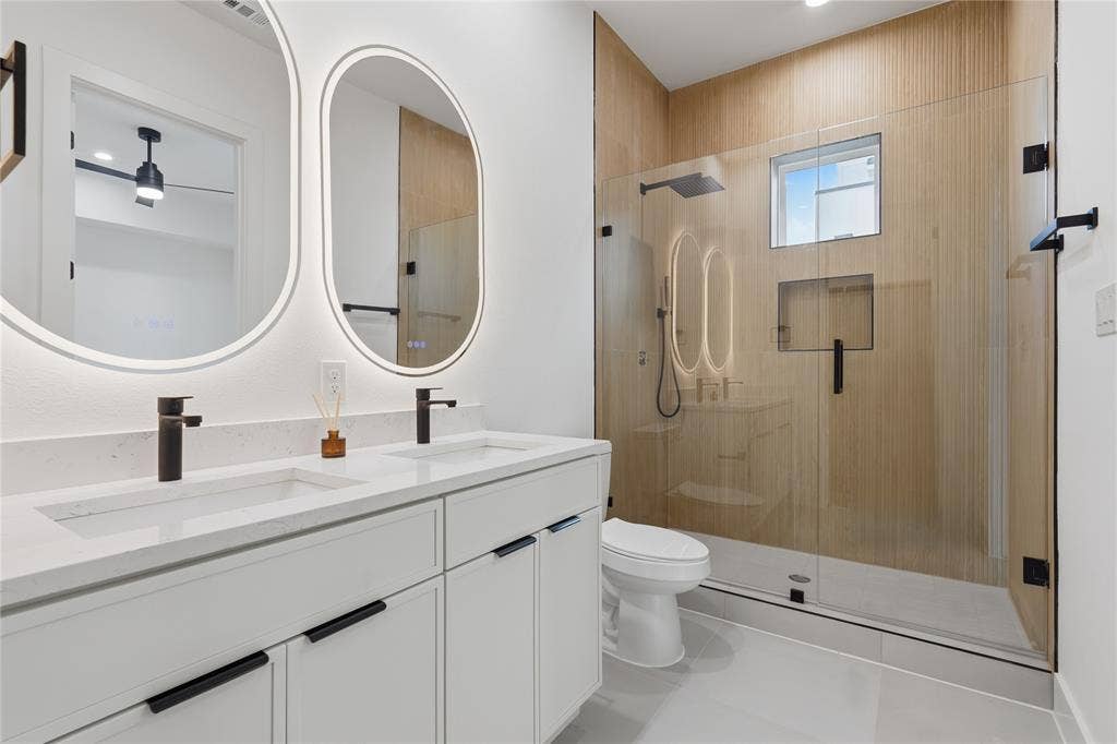 4319 San Jacinto Street, #101, Dallas, TX 75204 Double vanity featuring quartz countertops, matte black fixtures, illuminated oval mirrors, and a walk-in shower with wood-finish tile surround