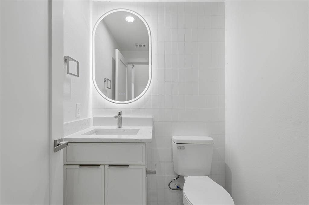4319 San Jacinto Street, #101, Dallas, TX 75204 Bathroom featuring a white vanity with a composite countertop, integrated rectangular sink, wall-mounted oval LED mirror, and tiled wall surround