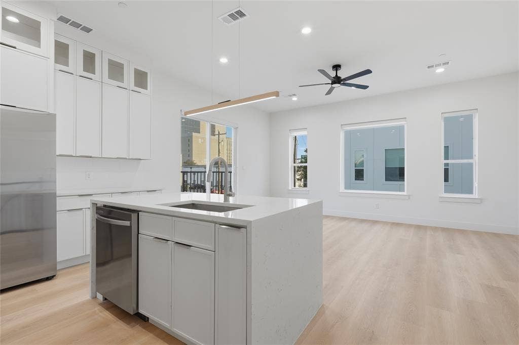 4319 San Jacinto Street, #101, Dallas, TX 75204 Kitchen featuring floor-to-ceiling white cabinetry, central island with stone-finish countertop, stainless steel appliance, wood-finish flooring, and recessed ceiling lighting