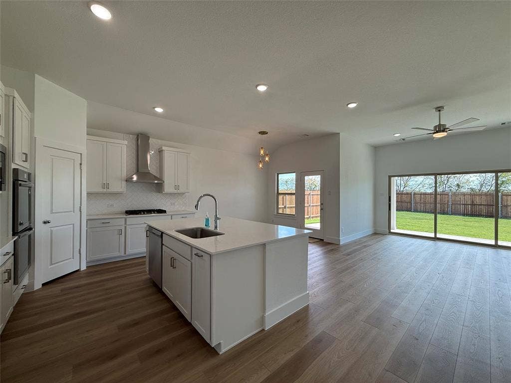 Kitchen featuring white shaker-style cabinetry, a central island with a quartz countertop, stainless steel appliances, wood-finish flooring, and large glass sliding doors