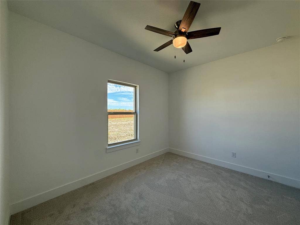 Neutral interior space featuring neutral wall-to-wall carpeting, a multi-blade dark wood-finish ceiling fan with integrated lighting, and a single window
