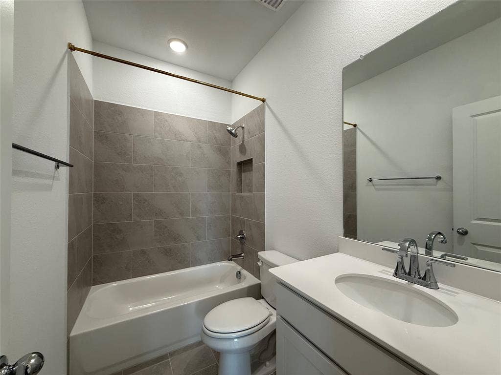 Bathroom featuring a vanity with a white countertop and oval under-mount sink, full-width mirror, and a tub-shower combination with grey tile surround and built-in recessed soap niche
