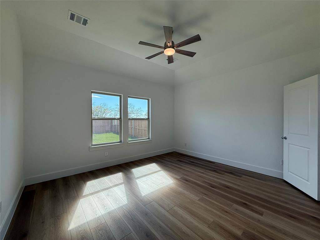 Room featuring wood-finish flooring, tray ceiling, central ceiling fan with integrated lighting, and dual windows