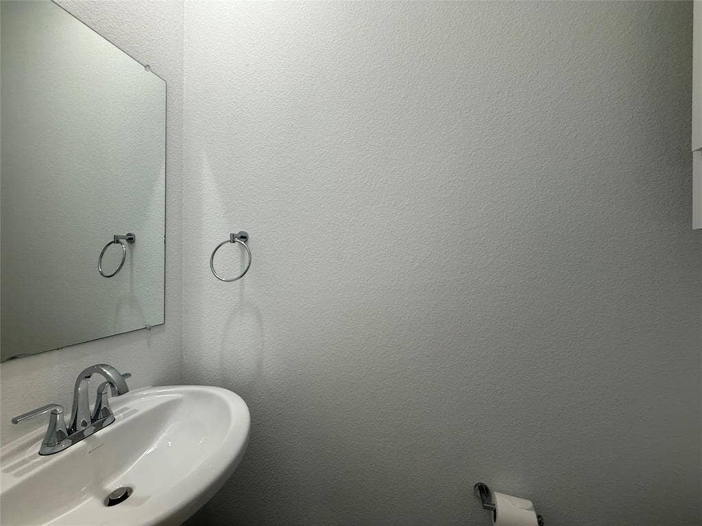 Wall-mounted frameless mirror, pedestal sink with a dual-handle chrome faucet, and circular metal towel ring