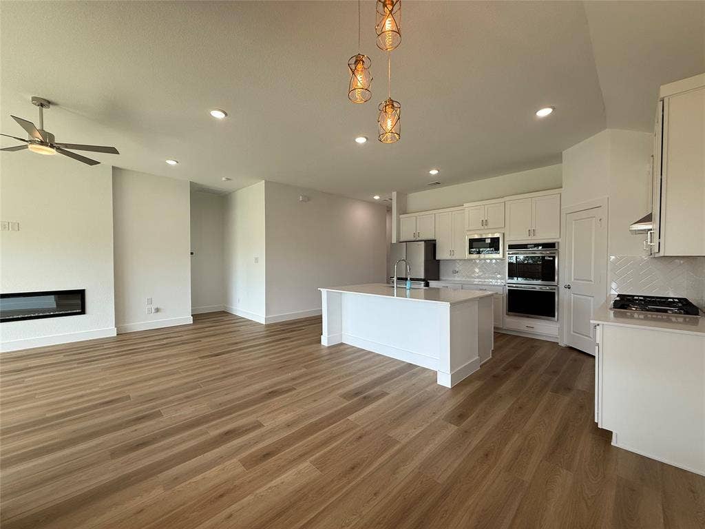 Open-concept living space featuring wood-finish flooring, a linear electric fireplace, a kitchen island, recessed lighting, and built-in stainless steel double ovens