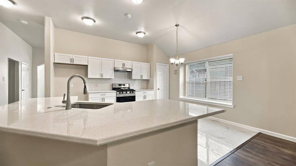 Kitchen featuring white cabinetry, solid surface countertops, a stainless steel range, undermount sink with a pull-down faucet, and vaulted ceilings